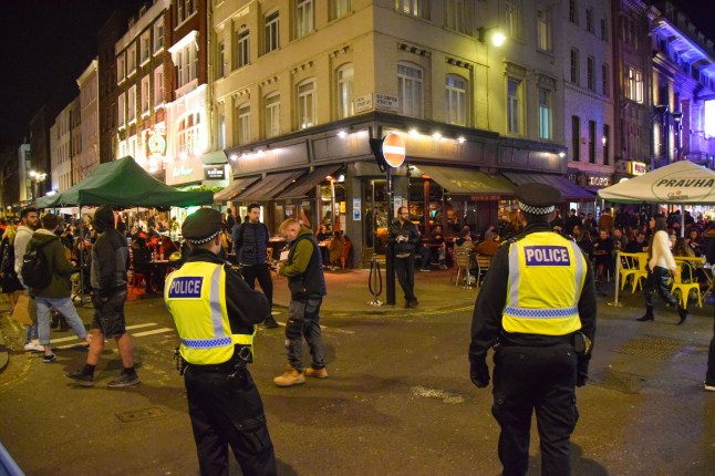London, United Kingdom - November 4 2020.Police officers and crowd of people on Old Compton Street, Soho at night. Temporary al fresco street seating was implemented to allow bars and restaurants to operate and facilitate social distancing during the coronavirus pandemic.