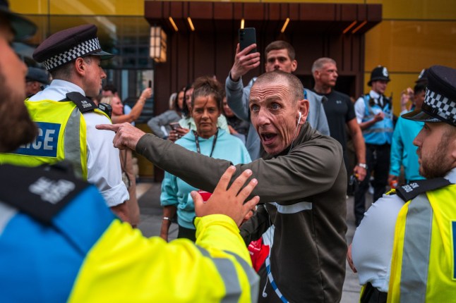 LONDON, ENGLAND - JULY 23: A man gestures next to a police officer during a protest outside the Britannia International Hotel in Canary Wharf on July 23, 2025 in London, England. A protest erupted here yesterday amid rumours - later confirmed by Tower Hamlets Council - of the government using the hotel to house asylum seekers. (Photo by Carl Court/Getty Images)