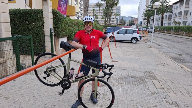 A man holding his bike against a railing for bicycle parking.